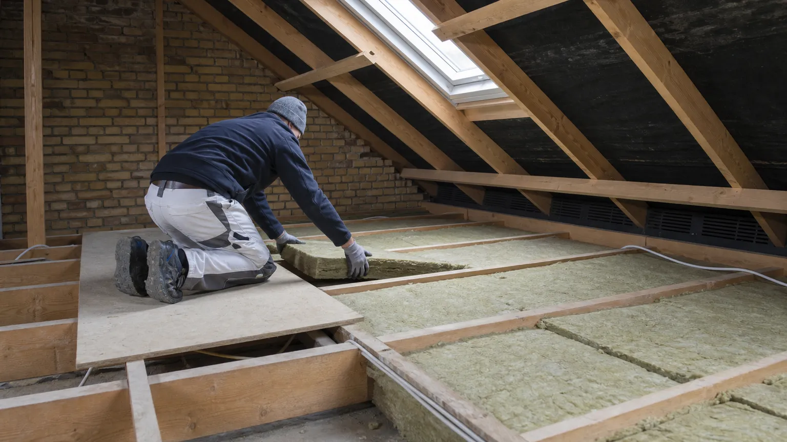 Håndværker lægger mineraluld mellem loftsbjælker i et dansk hus med naturligt dagslys.