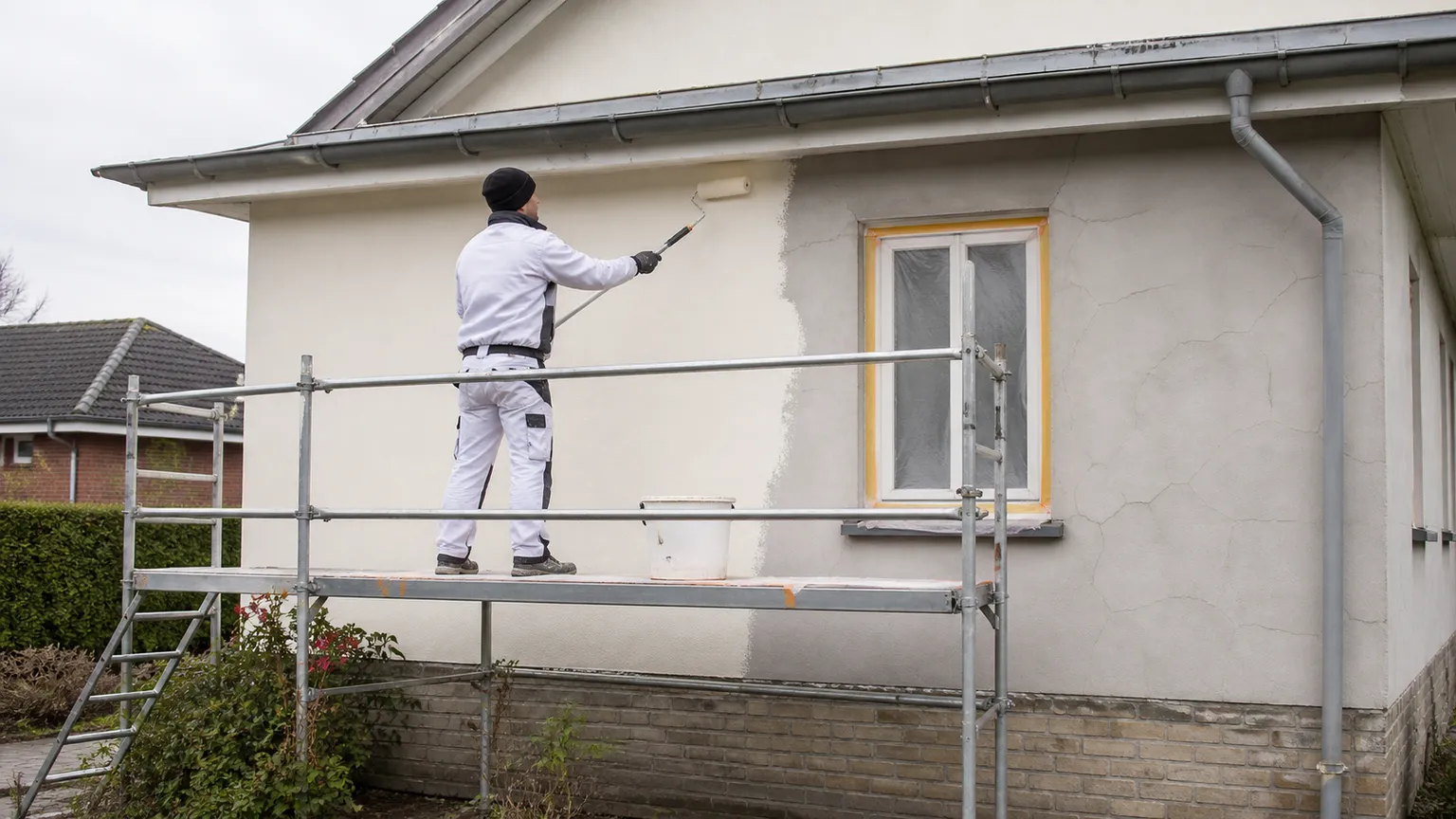 Professionel maler maler en dansk husfacade fra et sikkert stillads i blødt dagslys.