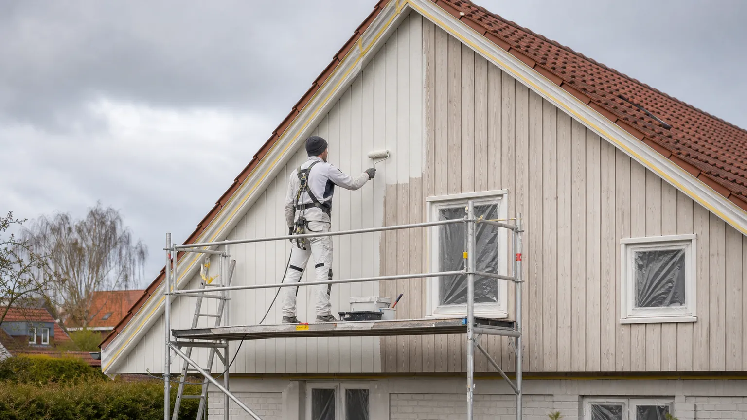 Maler på stillads maler trægavlen på et dansk hus i blødt dagslys.