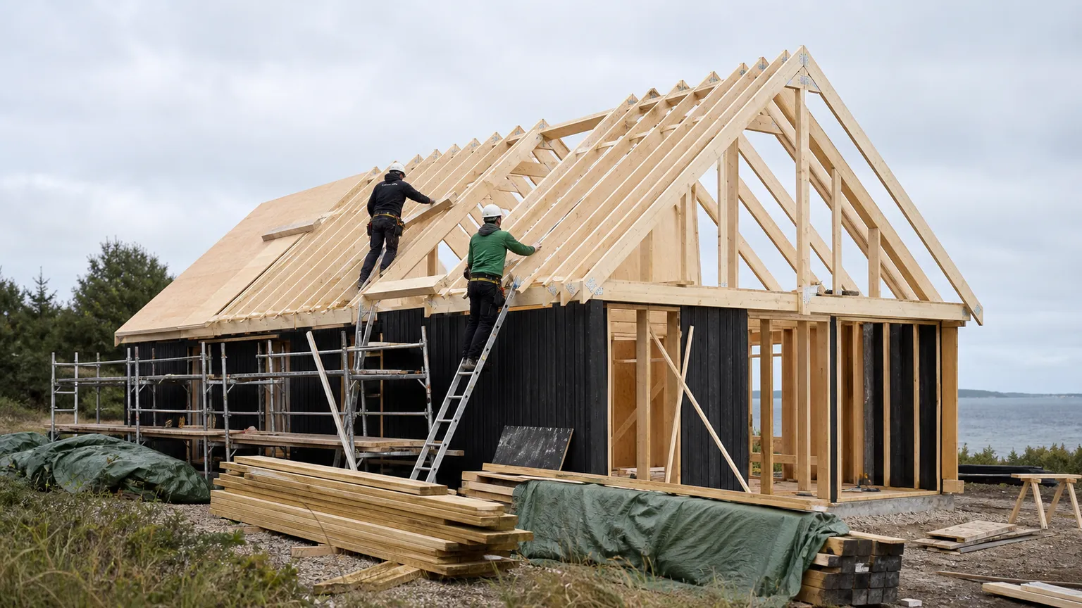 To tømrere monterer tagkonstruktionen på et sommerhus i træ ved den danske kyst.